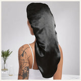 Une femme vue de dos portant un bonnet long en satin noir, dans un décor intérieur lumineux et minimaliste