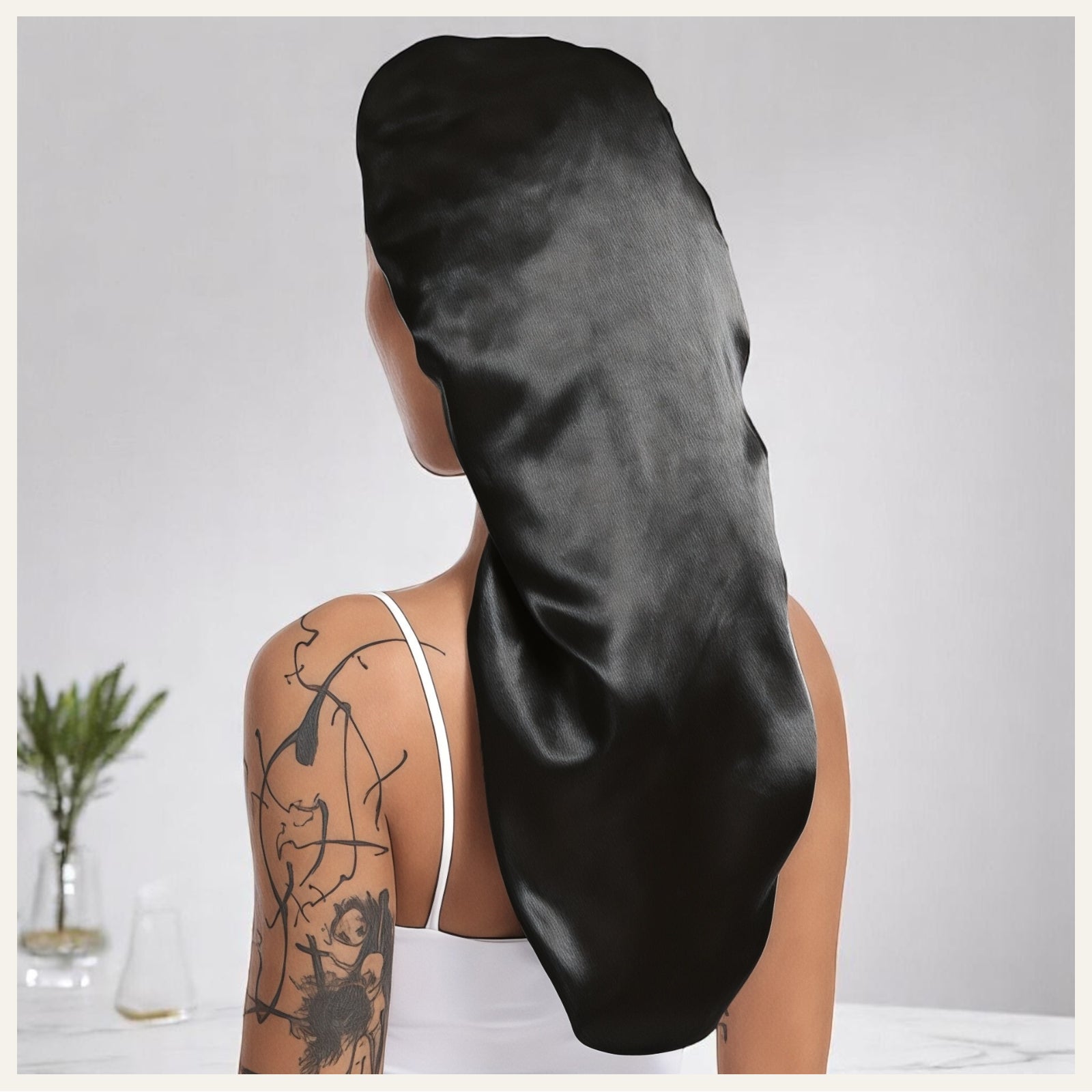 Une femme vue de dos portant un bonnet long en satin noir, dans un décor intérieur lumineux et minimaliste