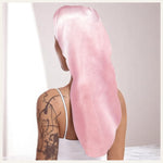 Une femme vue de dos portant un bonnet long en satin rose, sur fond intérieur doux et lumineux