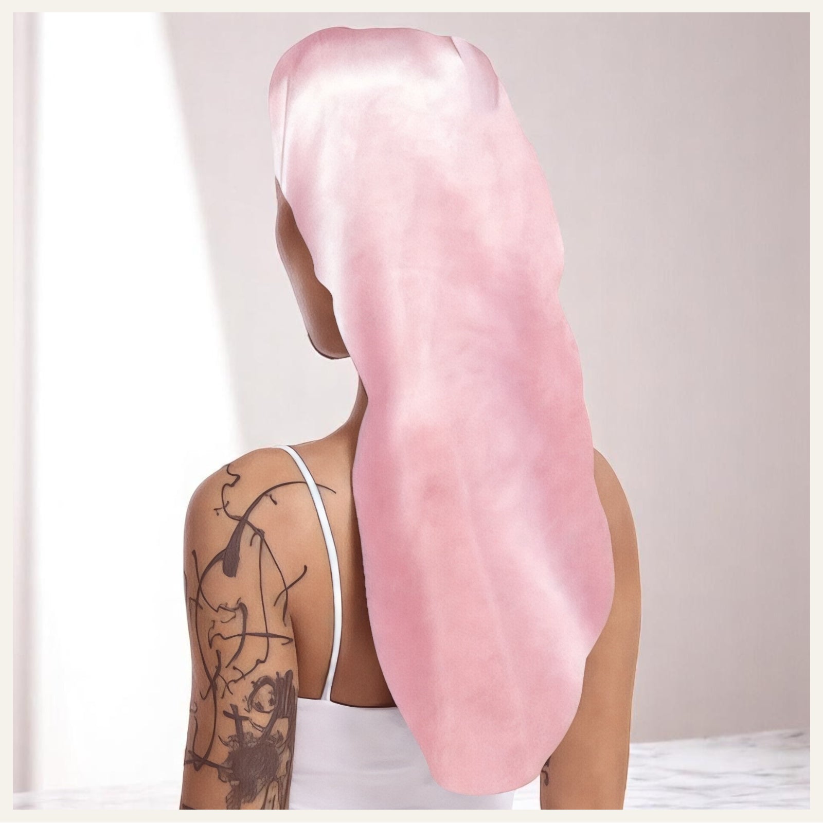 Une femme vue de dos portant un bonnet long en satin rose, sur fond intérieur doux et lumineux