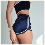 Une femme portant un pyjama short en satin bleu marine à bordures blanches, posant de profil dans un intérieur lumineux