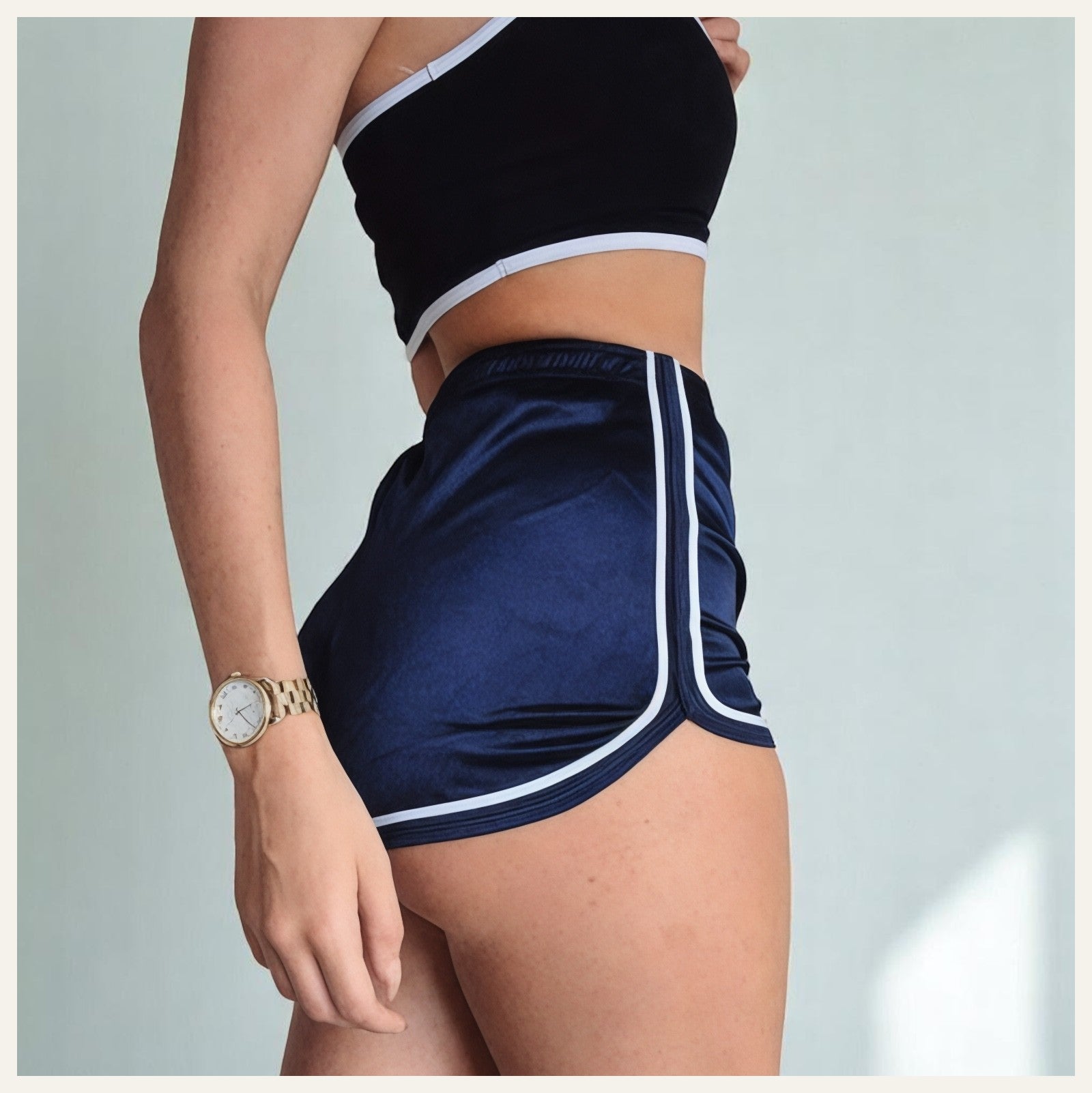 Une femme portant un pyjama short en satin bleu marine à bordures blanches, posant de profil dans un intérieur lumineux