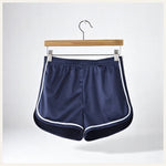 Un short de pyjama en satin bleu marine avec liserés blancs, suspendu sur un cintre en bois contre un fond clair