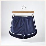 Un short de pyjama en satin bleu marine avec liserés blancs, suspendu sur un cintre en bois contre un fond clair