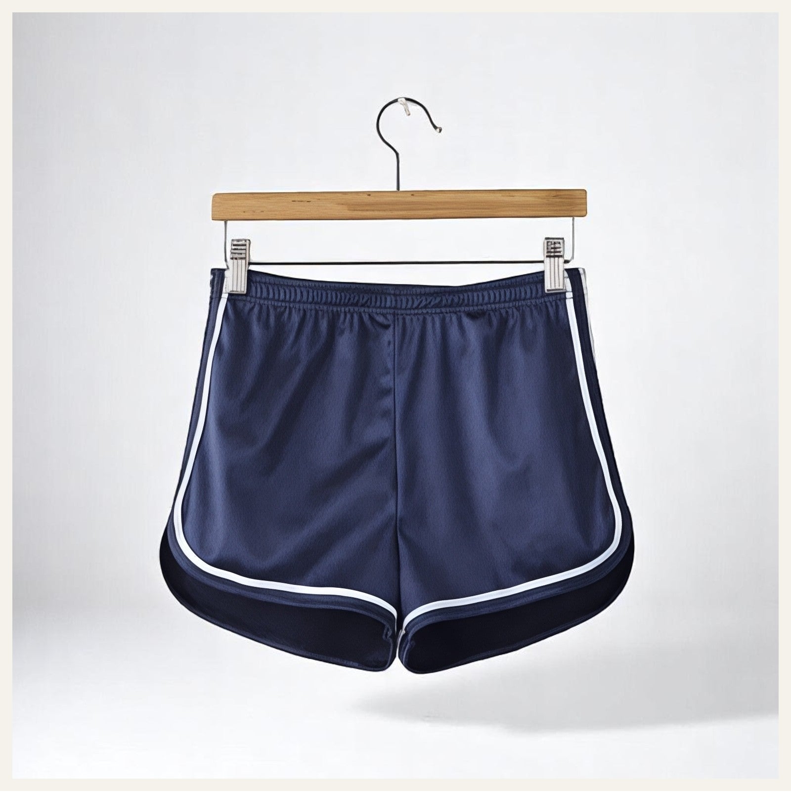 Un short de pyjama en satin bleu marine avec liserés blancs, suspendu sur un cintre en bois contre un fond clair