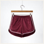 Un short de pyjama en satin rouge bordeaux avec liserés blancs, suspendu sur un cintre en bois contre un fond blanc