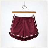 Un short de pyjama en satin rouge bordeaux avec liserés blancs, suspendu sur un cintre en bois contre un fond blanc