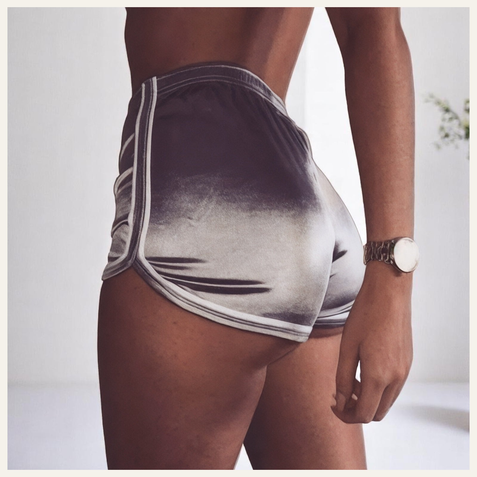 Une femme portant un pyjama short en satin gris dégradé, photographiée de dos dans un intérieur lumineux et épuré