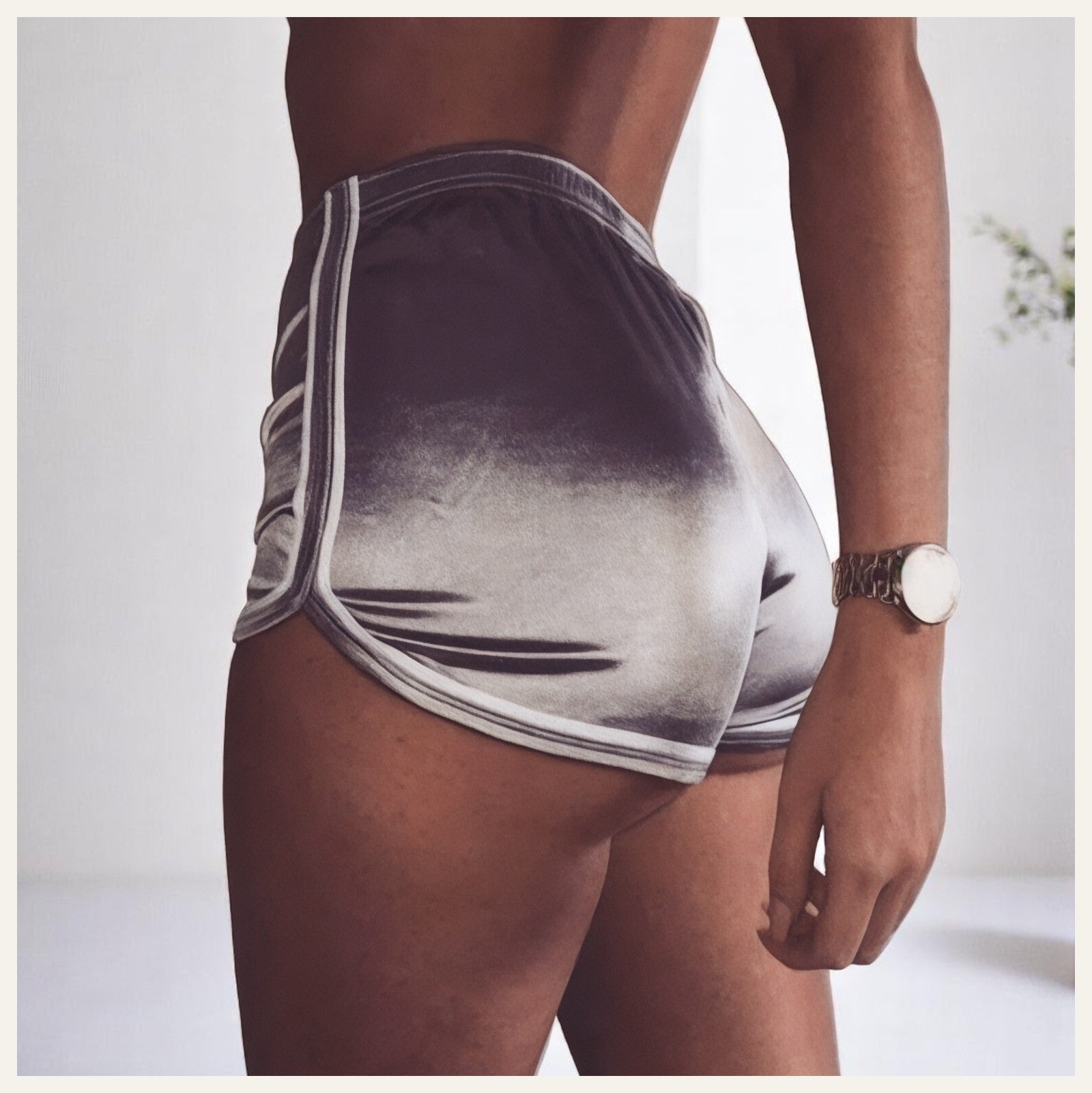 Une femme portant un pyjama short en satin gris dégradé, photographiée de dos dans un intérieur lumineux et épuré