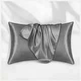 une taie d'oreiller en satin gris élégamment disposée sur un fond blanc, mettant en valeur sa douceur et son éclat raffiné.